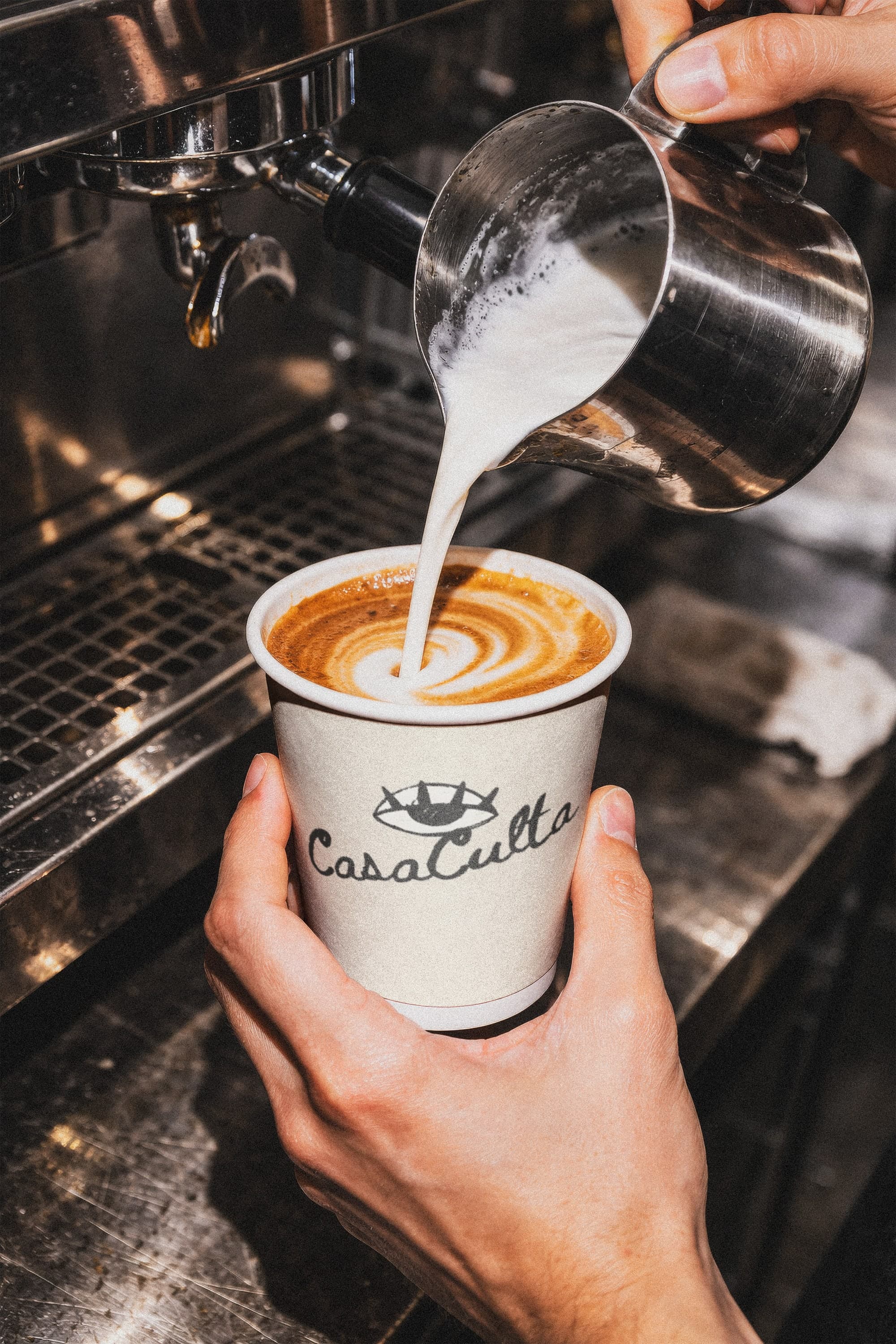 Barista pouring latte art into a Casa Culta takeaway cup