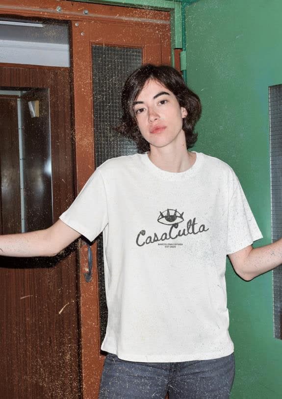 Person wearing a white Casa Culta logo t-shirt in a green doorway
